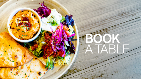 A plate of colourfull food with bread on the side and the words Book a Table